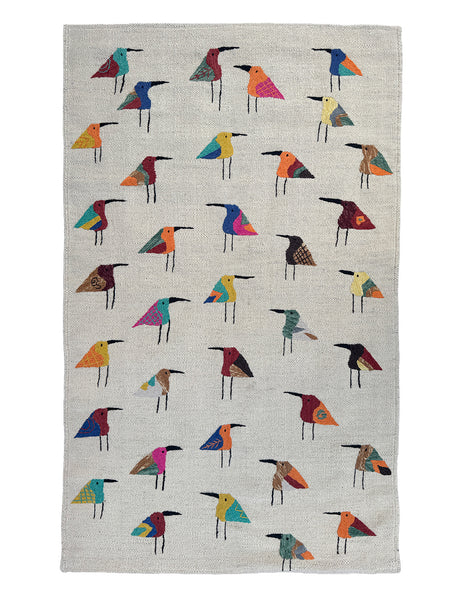 A woven Suzani rug with a light ecru linen-like background, decorated with rows of stylised bird figures in many different colours including blue, red, yellow, orange, green, and black.