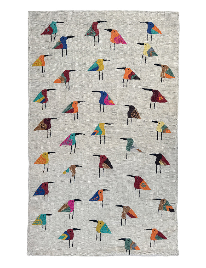 A woven Suzani rug with a light ecru linen-like background, decorated with rows of stylised bird figures in many different colours including blue, red, yellow, orange, green, and black.