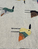 Close-up of a woven suzani rug with a cream base and embroidered bird motifs in muted green, mustard yellow, orange, brown, and black.